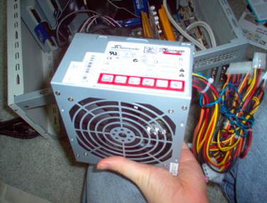 Photograph of PSU with power cables coming out of the back. It is held in a person’s hand. Photograph of PSU with power cables coming out of the back. It is held in a person’s hand.