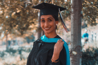 a woman posing for a photo wearing a graduation cap and gown under a tree